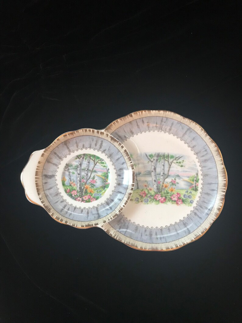 Pu&ograve; includere: Un set di due piatti in ceramica vintage con un design di betulla grigio e bianco. I piatti hanno un bordo a festoni e un bordo dorato.