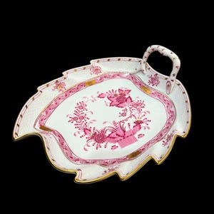 May include: A white porcelain serving tray with a pink floral design and a gold rim. The tray is shaped like a leaf and has a handle.