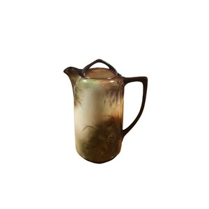 Peut inclure: Une théière en céramique brune et verte avec un motif floral. La théière a un couvercle et une poignée.