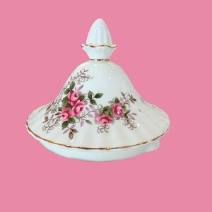 Peut inclure: Couvercle en porcelaine blanche avec un motif floral de roses roses et vertes. Le couvercle a une bordure dorée et un bouton décoratif. Le couvercle est probablement pour une théière ou un plat de service.