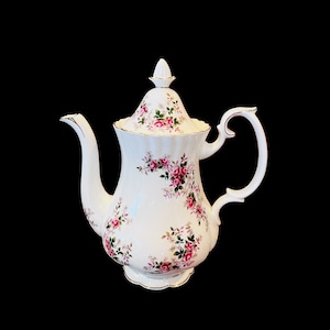 May include: White porcelain teapot with a floral pattern of pink and green roses. The teapot has a lid with a knob on top and a handle on the side.