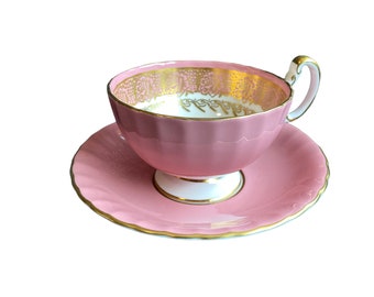 May include: A pink teacup and saucer set with gold trim and a delicate floral pattern. The cup has a fluted design and a white interior.