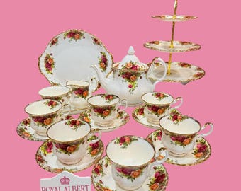 May include: A Royal Albert tea set featuring white porcelain with red and yellow rose patterns and gold trim. The set includes a teapot, a three-tier cake stand, a creamer, and multiple teacups with matching saucers. A sign reads ROYAL ALBERT MADE IN ENGLAND.