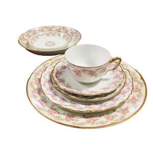 May include: A set of vintage porcelain teacups and saucers with a delicate floral pattern in shades of pink and green. The set features a cup, saucer, and a small bowl with a gold rim.