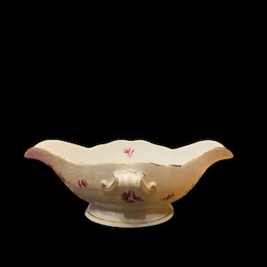 Peut inclure: Un saucier en porcelaine blanche avec un bord doré et un motif floral rose.