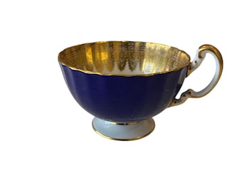May include: A blue and gold teacup with a white base and a gold rim. The cup has a scalloped edge and a delicate floral pattern.