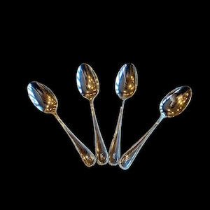 May include: Four silver spoons with beaded edges, arranged in a fan shape against a black background.