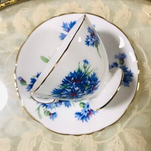 May include: A white teacup and saucer with a blue and white floral pattern. The cup and saucer have a gold trim.