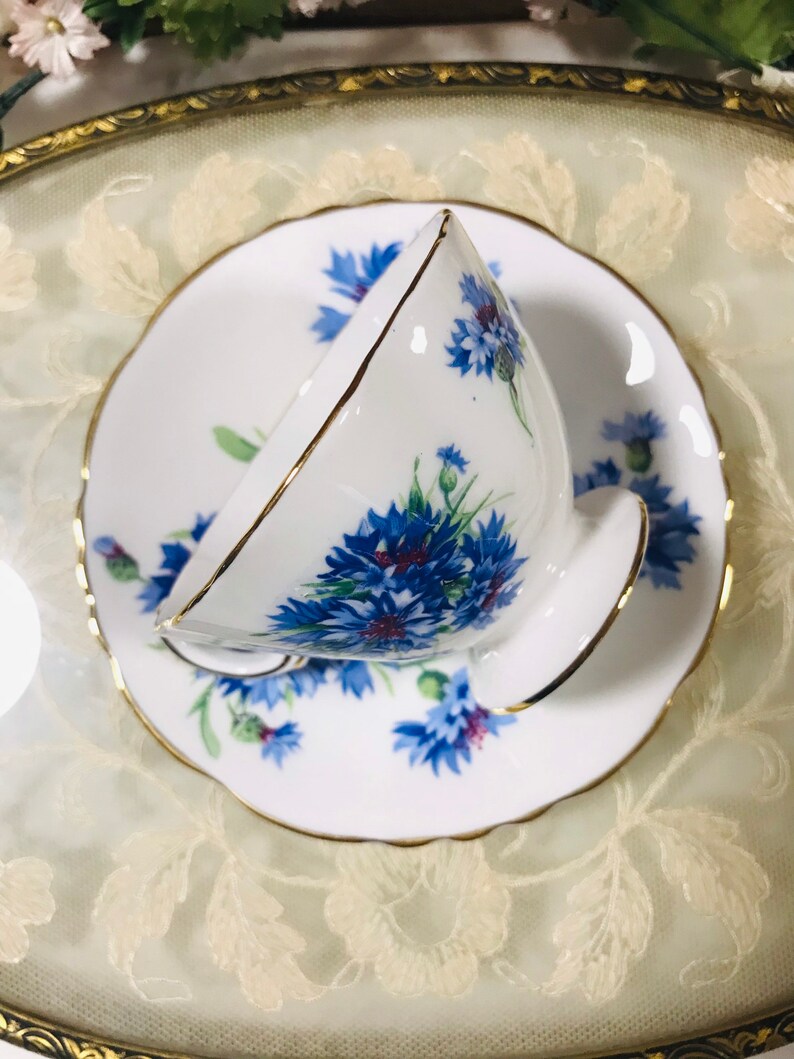 May include: A white teacup and saucer with a blue and white floral pattern. The cup and saucer have a gold trim.