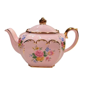 May include: A pink teapot with a floral design and gold accents. The teapot has a scalloped edge and a lid with a knob.
