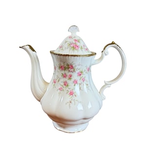 Peut inclure: Une théière en porcelaine blanche avec un couvercle, ornée de motifs floraux de roses roses et de bordures dorées. La théière présente un bec et une anse incurvés, ainsi qu'un bouton décoratif sur le couvercle. Une pièce classique pour servir le thé.