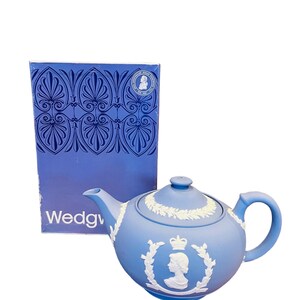 Op de afbeelding: Een blauwe Wedgwood-theepot met een wit reliëfdesign van koningin Elizabeth II. De theepot zit in de originele doos.