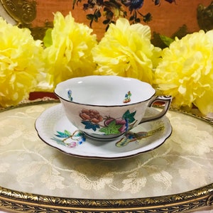 May include: A white porcelain teacup and saucer with a floral pattern. The cup has a delicate handle and a scalloped rim. The saucer has a matching floral pattern and a gold trim.