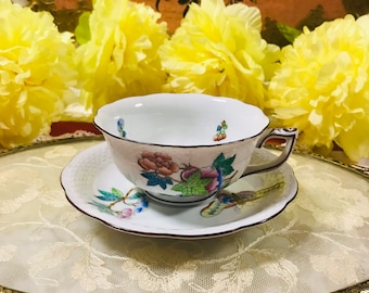 May include: A white porcelain teacup and saucer with a floral pattern. The cup has a delicate handle and a scalloped rim. The saucer has a matching floral pattern and a gold trim.