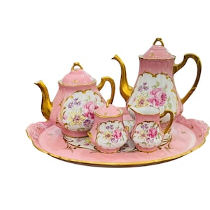 May include: A pink porcelain tea set with gold detailing, comprising a teapot, sugar bowl, creamer, and cups, adorned with floral designs. The set is presented on a matching pink tray.