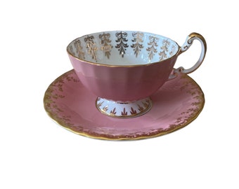 May include: A pink teacup and saucer set with gold trim and a delicate floral pattern. The cup and saucer are made of fine china and have a vintage aesthetic.