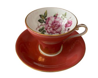 May include: A red teacup and saucer set with a floral design. The cup has a white interior with a pink rose and green leaves. The saucer is a solid red color with a gold trim.
