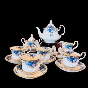 Puede incluir: Un juego de té vintage con un patrón de rosas azules. El juego incluye una tetera, una jarra de crema, un azucarero y cuatro tazas de té y platillos.