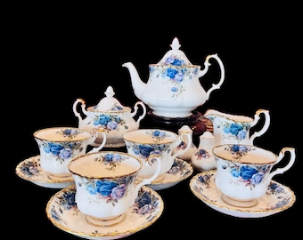 May include: A vintage tea set featuring a blue rose pattern. The set includes a teapot, creamer, sugar bowl, and four teacups and saucers.