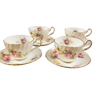 May include: Set of four white teacups and saucers with a floral pattern in shades of pink, yellow, and blue. The cups and saucers have a gold trim.