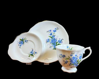 May include: A vintage teacup, saucer, and serving plate set. The white porcelain pieces feature a delicate blue floral pattern with gold trim. The set includes a teacup, a small saucer, and a two-part serving plate.
