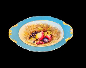 May include: A blue and white oval serving dish with a gold rim. The dish features a painted design of fruit, including grapes, pears, plums, and raspberries.