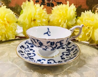 May include: A white teacup and saucer with a blue and gold floral pattern. The teacup and saucer are on a gold tray with a white lace overlay.
