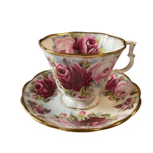 Puede incluir: Una taza de té y un platillo blancos con un patrón floral de rosas rosas y rojas y un borde dorado.