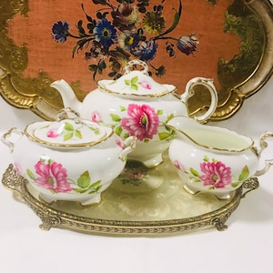 May include: A white tea set with pink floral designs on a gold tray. The set includes a teapot, creamer, and sugar bowl.