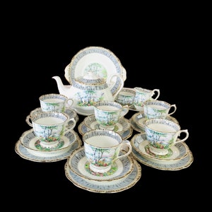 May include: A vintage tea set with a floral pattern. The set includes a teapot, six cups and saucers, and a serving plate. The cups and saucers have a delicate floral design with a blue and green color scheme. The teapot has a matching floral design and a gold trim.