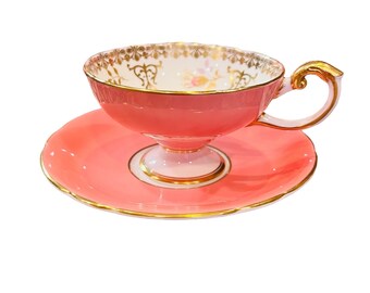 May include: A pink teacup and saucer set with gold trim and floral details.