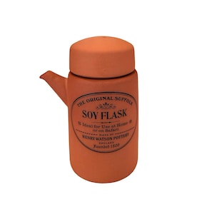 May include: A terracotta-colored soy flask with a rounded lid and a spout. The flask has a label that reads "THE ORIGINAL SUFFOLK SOY FLASK" and "HENRY WATSON POTTERY ENGLAND Founded 1800".