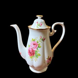 May include: White porcelain coffee pot with a lid, decorated with pink and red roses and green leaves. The pot has a curved spout, a handle, and gold trim. The pot is approximately 20 cm in height.