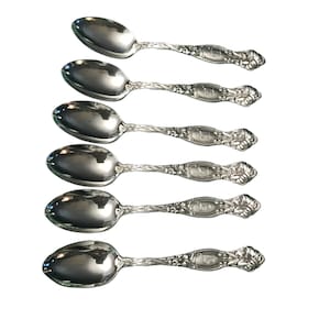 Puede incluir: Juego de seis cucharaditas de plata con mangos adornados. Cada cuchara tiene un diseño floral y la inscripción "1900" en la parte posterior.