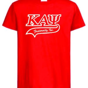Może przedstawiać: Jaskrawoczerwony t-shirt z krótkim rękawem z białą grafiką na klatce piersiowej. Grafika przedstawia napis "KAY" pogrubioną, stylizowaną czcionką z grecką literą Psi, a pod nim kursywą napis "Fraternity, Inc." podkreślony ozdobną linią.