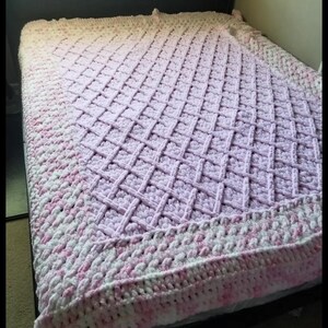 Puede incluir: Una manta de ganchillo en punto de rejilla de diamante con doble borde. La manta est&aacute; hecha con un hilo degradado en tonos de blanco y rosa.