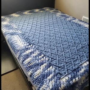 Puede incluir: Una manta de crochet azul y blanca con un punto de rejilla de diamante y un doble borde. El borde est&aacute; hecho con un punto de torsi&oacute;n de liga y un punto de cadena. La manta est&aacute; hecha con dos tonos de azul, azul campo y azul denim.