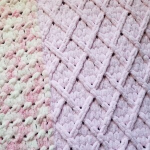 Puede incluir: Una manta de crochet suave, rosa y blanca con un patr&oacute;n de diamante. La manta est&aacute; hecha con un hilo esponjoso y tiene una textura suave y peluda.