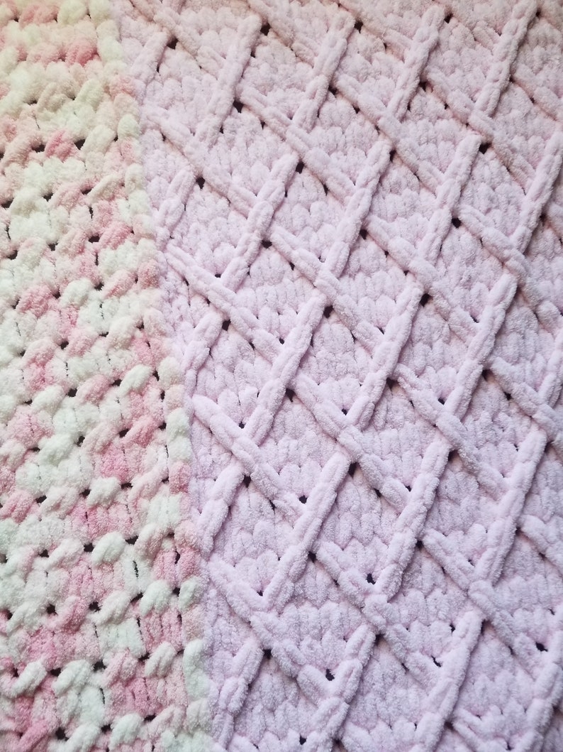 Puede incluir: Una manta de crochet suave, rosa y blanca con un patr&oacute;n de diamante. La manta est&aacute; hecha con un hilo esponjoso y tiene una textura suave y peluda.