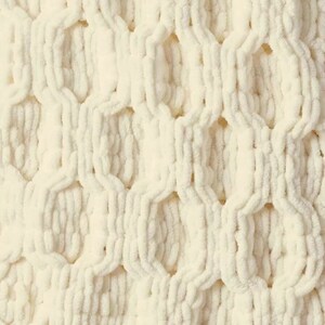 Puede incluir: Primer plano de una tela blanca tejida con un patr&oacute;n de punto de nido de abeja. La tela es suave y esponjosa, y el punto crea una superficie texturizada.