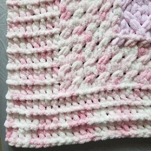 Puede incluir: Una manta de beb&eacute; de crochet rosa y blanca con una textura esponjosa.
