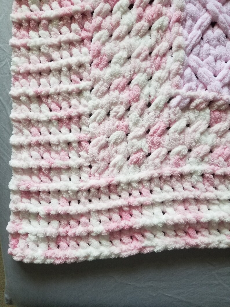 Puede incluir: Una manta de beb&eacute; de crochet rosa y blanca con una textura esponjosa.