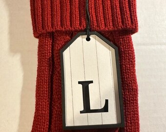 May include: Red knitted cable knit stocking with a white tag that says "L" on it.