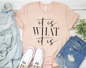 May include: A peach-colored t-shirt with the text "it is WHAT it is" printed in black.