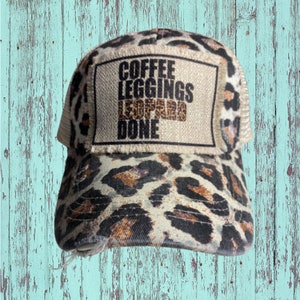 May include: A distressed baseball cap with a leopard print pattern and a mesh back. The front patch reads "Coffee, Leggings, Leopard, Done" in black and brown lettering. The hat has a pre-worn, vintage look.