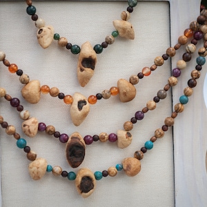 Op de afbeelding: Drie gelaagde kettingen met bruine, beige en groene kralen. De kettingen hebben unieke, onregelmatig gevormte, lichtbruine stenen hangers.