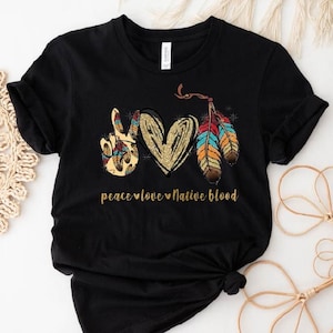 May include: Black t-shirt with a peace sign, heart, and feathers. The text "peace love Native blood" is printed on the shirt.