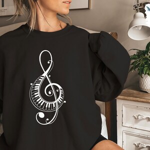 Peut inclure: Sweat-shirt noir avec un motif de cl&eacute; de sol blanche int&eacute;grant un clavier de piano.