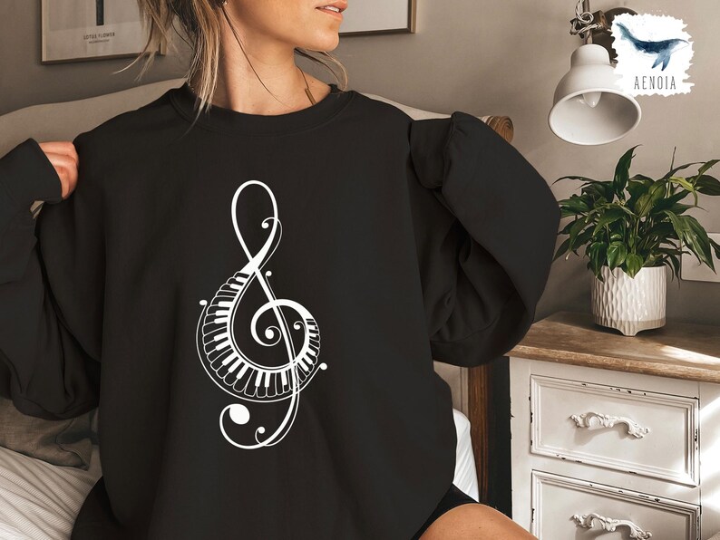 Peut inclure: Sweat-shirt noir avec un motif de cl&eacute; de sol blanche int&eacute;grant un clavier de piano.