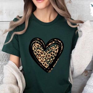 Puede incluir: Una camiseta verde oscuro con un gran gr&aacute;fico de coraz&oacute;n con contorno negro. El coraz&oacute;n est&aacute; relleno con un patr&oacute;n de estampado de leopardo.